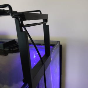 May include: Black metal aquarium light fixture with a clip-on design. The light is mounted on the top of a glass aquarium.