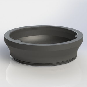 May include: A black plastic ring with a beveled edge and a small opening on the top. The ring is designed to fit around a bottle or jar.