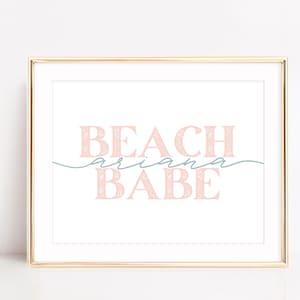 Może przedstawiać: Druk w złotej ramie z tekstem "BEACH ariana BABE" w kolorze różowym z kwiatowym wzorem. Tekst "ariana" jest mniejszą czcionką i w jasnoniebieskim kolorze.