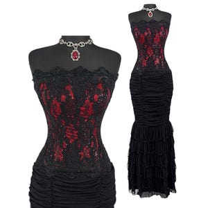 May include: A strapless floor-length dress featuring a black lace overlay with red fabric underneath, a ruched bodice, and a tiered ruffled skirt. The dress is paired with a silver-toned choker necklace featuring a central red oval stone.