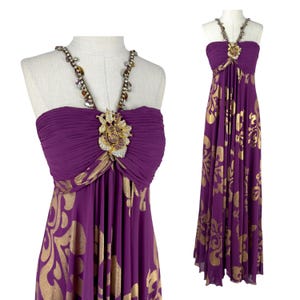 Könnte beinhalten: Ein bodenlanges violettes Kleid mit goldenem Damastmuster, einem plissierten Oberteil und einem Neckholder-Ausschnitt, der mit einer großen, mit Juwelen besetzten Blumenbrosche und perlenbesetzten Trägern verziert ist.