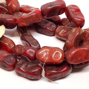 May include: A strand of red and gold nugget-shaped beads. The beads are made of glass and have a shiny, iridescent finish.