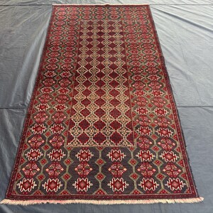 Puede incluir: Una alfombra persa tradicional con un patrón geométrico en tonos rojos, azules y crema. La alfombra tiene un borde con flecos y está hecha de lana.