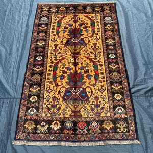 May include: A traditional Persian rug with a yellow background and intricate floral patterns in shades of red, blue, green, and brown. The rug has a dark brown border with a repeating floral motif.