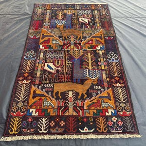May include: A colorful rug with a geometric design featuring stylized trees, animals, and flowers. The rug has a dark background with bright red, yellow, blue, and green accents.