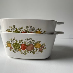 May include: Two white ceramic baking dishes with a floral pattern featuring green leaves, red and yellow peppers, and artichokes. The dishes are stacked on top of each other. The bottom dish has the number "40" printed on the bottom.