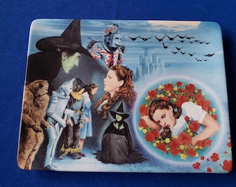 May include: A ceramic plate with a colorful image of characters from the Wizard of Oz. The plate features Dorothy, the Wicked Witch of the West, the Scarecrow, the Tin Man, the Cowardly Lion, and the flying monkeys. The plate is a light blue color with a white border.