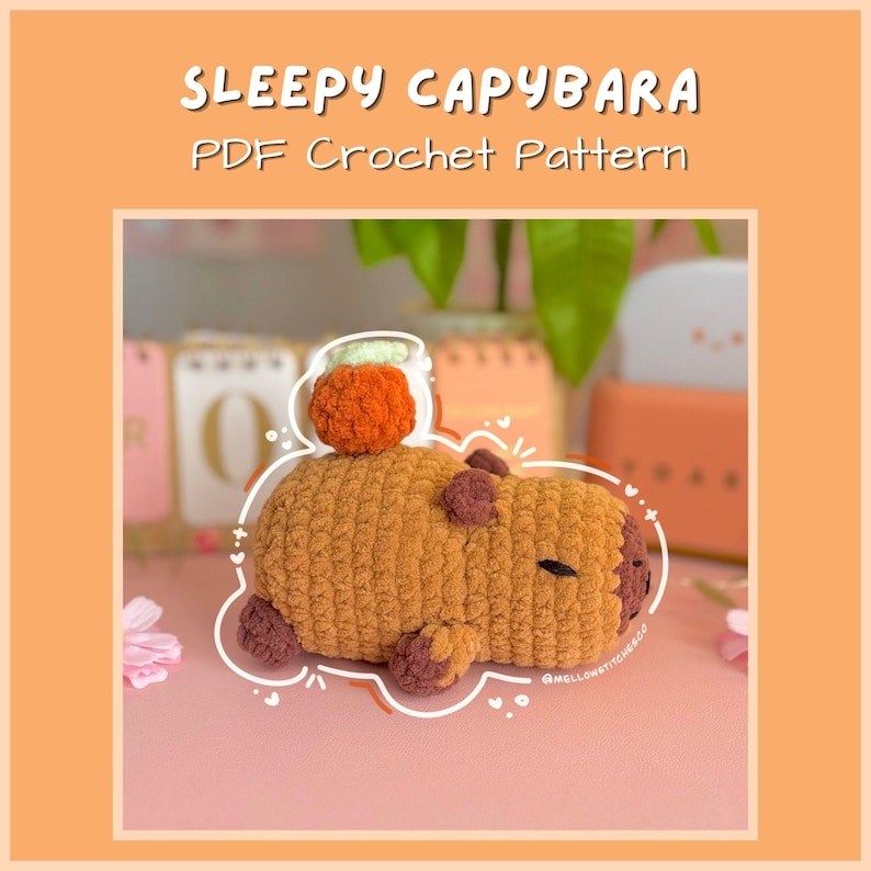 May include: A crocheted capybara plushie in shades of brown and tan, with a small orange pumpkin on its head. The text "SLEEPY CAPYBARA PDF Crochet Pattern" is displayed above the plushie. The plushie is lying on a pink surface.