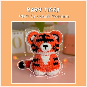 May include: A crocheted baby tiger in orange, black, and white. The tiger has a cute, rounded design with a white belly and paws. The text "BABY TIGER PDF Crochet Pattern" is displayed above the tiger.