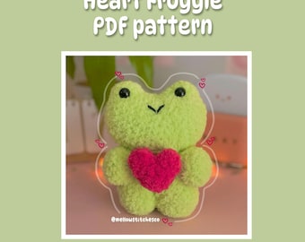 May include: A green crocheted frog holding a pink heart. The frog is surrounded by pink hearts. The text "@mellowstitchesco" is at the bottom of the image.
