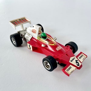 Puede incluir: Coche de carreras de juguete rojo y blanco con un conductor, el coche tiene las palabras "Texaco" y "Marlboro" en él, y el número "5" en el lateral.