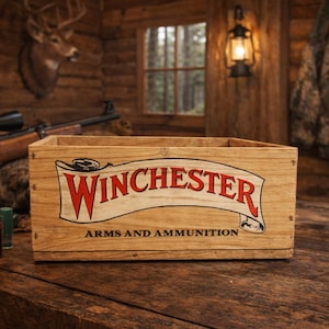 May include: Wooden box with the Winchester logo in red and white, with the words "ARMS AND AMMUNITION" below. The box is on a wooden surface, with a rifle and ammunition visible in the background. The scene is set in a rustic cabin.