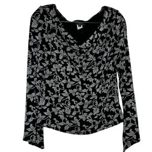 May include: A long-sleeved top featuring a black base with a shimmering silver floral pattern throughout. The garment has a draped cowl neckline and a straight hemline, with a visible brand label located at the interior back of the collar.