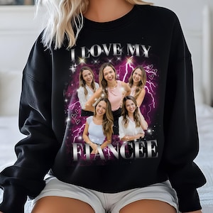 Pu&ograve; includere: Felpa nera con il testo "I love my fiancee" in lettere argentate glitter. La felpa presenta una grafica rosa e viola con fulmini e cuori. Ci sono cinque foto di donne nella grafica.