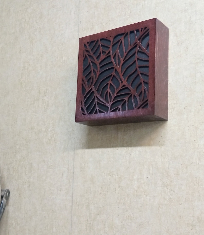May include: A dark brown wooden wall mounted box with a leaf pattern cut out design. The box has a black background.