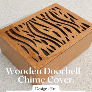 May include: A rectangular wooden doorbell chime cover with a laser-cut design on the top. The cover is made of light brown wood and features a series of curved, wave-like cutouts. The text "Wooden Doorbell Chime Cover" and "Design: En" are visible.