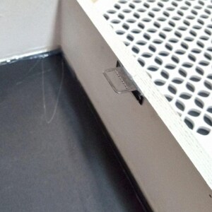 May include: Close-up of a corner of a white, patterned surface with a metal latch. The surface has a repeating design of rounded shapes. The latch is rectangular and attached to the side of the surface.