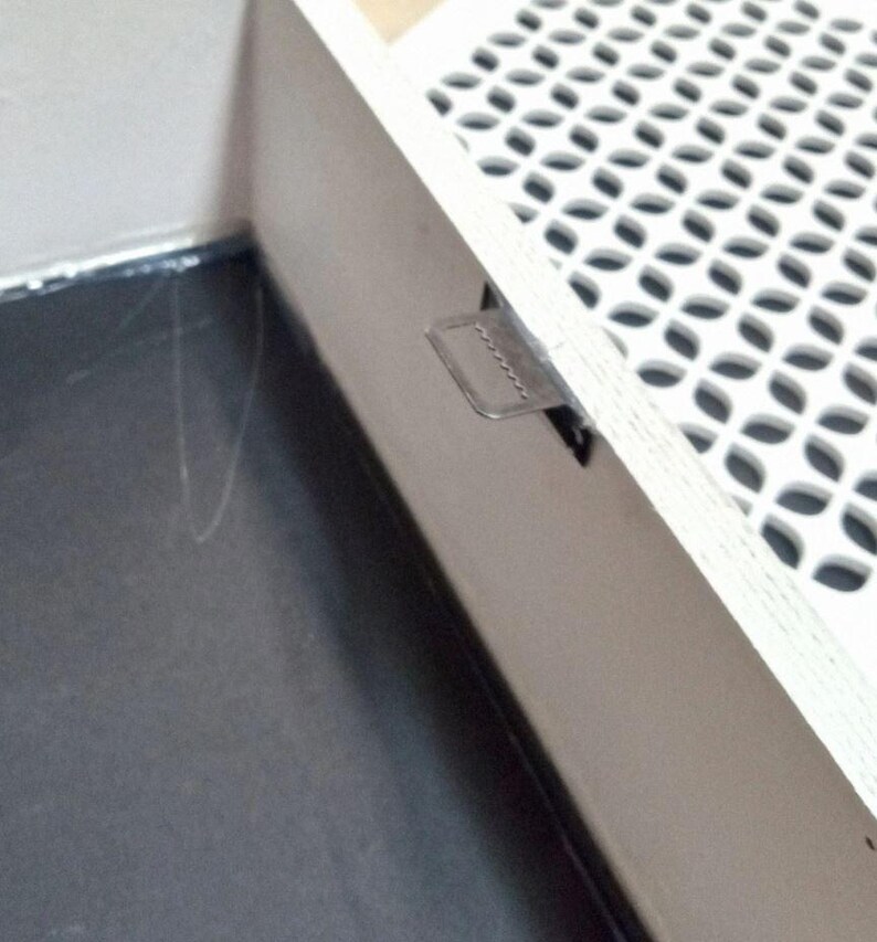 May include: Close-up of a corner of a white, patterned surface with a metal latch. The surface has a repeating design of rounded shapes. The latch is rectangular and attached to the side of the surface.