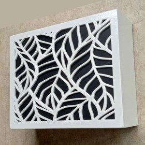 May include: White wooden box with a black background and a cut-out design of white leaves.