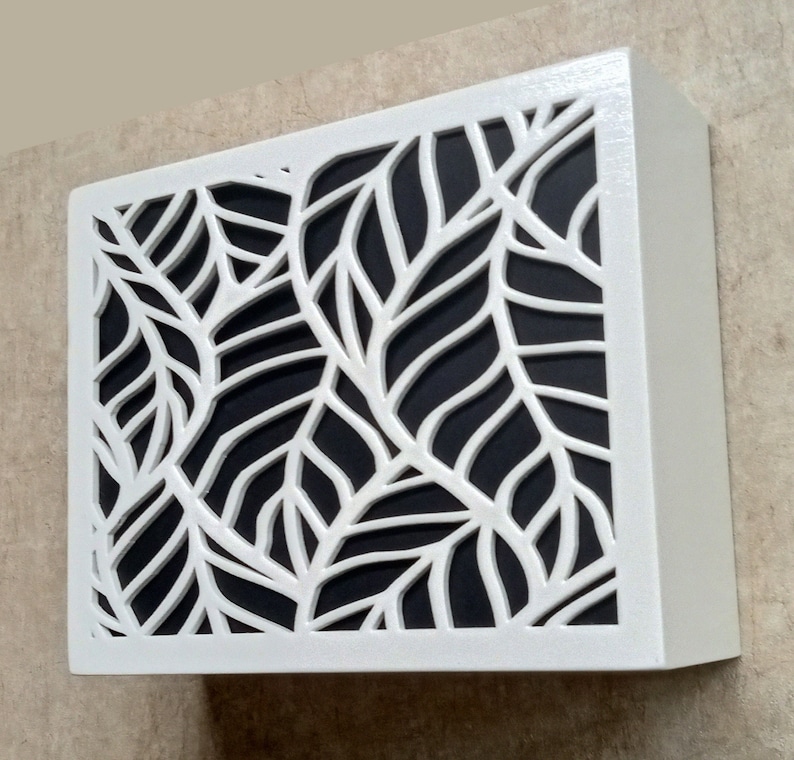 May include: White wooden box with a black background and a cut-out design of white leaves.