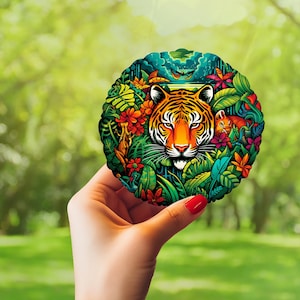 Puede incluir: Una pegatina redonda colorida con un tigre con follaje verde, azul y rojo. El tigre tiene rayas naranjas y negras y un fondo blanco.