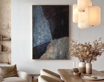 May include: An abstract painting with a gold frame, featuring shades of blue, black, and beige. The artwork hangs above a wooden dining table with beige chairs. A cream-colored armchair and a modern light fixture complete the room's decor.