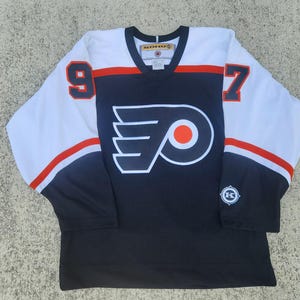 May include: A black and white hockey jersey with the Philadelphia Flyers logo and the numbers 9 and 7 on the front. The jersey has red and orange accents.