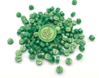 May include: A large pile of green wax sealing beads with a single gold leaf wax seal in the centre. The wax seal features a gold leaf design of a branch with leaves.