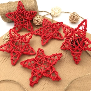 Puede incluir: Cinco estrellas rojas tejidas de mimbre. Las estrellas están dispuestas sobre una superficie marrón con cuerda y pequeñas bolas blancas y marrones.