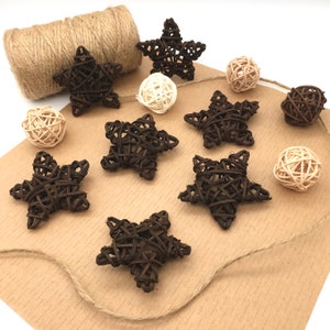 Op de afbeelding: Een verzameling van bruine geweven sterornamenten en witte geweven balornamenten op een bruine papieren achtergrond. De ornamenten zijn aan elkaar gebonden met touw.