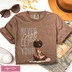 Könnte beinhalten: Espressofarbenes T-Shirt mit dem Text "Never Let Your Crown Tilt" und einer Illustration einer Frau mit Krone. Das Shirt ist mit Sonnenbrille, Hut und Jeans gestylt.