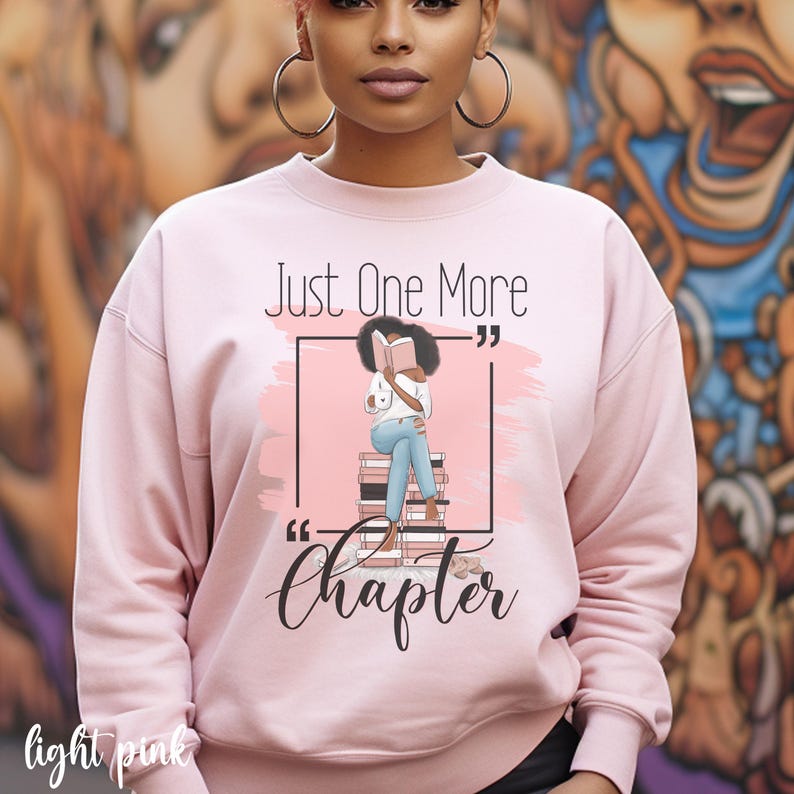 May include: Light pink sweatshirt with the text "Just One More Chapter." The graphic features a person reading a book while sitting on a stack of books. The words "light pink" are written at the bottom left of the sweatshirt.