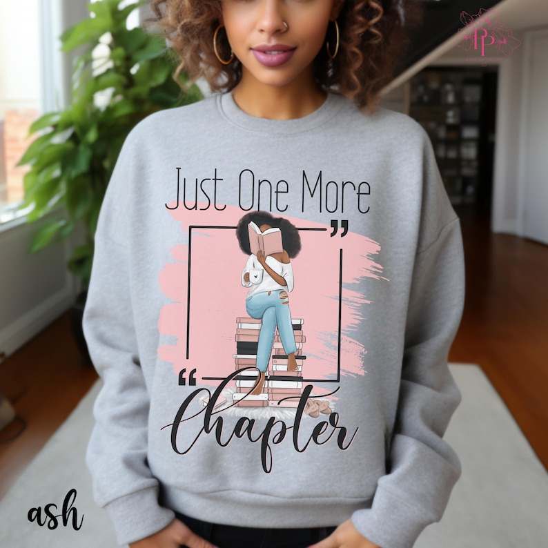 May include: Ash gray sweatshirt with the text "Just One More Chapter" and an illustration of a person reading a book. The graphic includes a pink background and a stack of books. The word "ash" is printed at the bottom left.