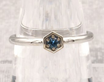 Puede incluir: Un anillo de plata con una piedra preciosa azul engastada en un bisel hexagonal. El anillo está en un expositor transparente.