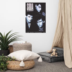 May include: A black and white rectangular poster featuring three men in a portrait arrangement with the text SODA STEREO at the top and GIRA NADA PERSONAL '85 at the bottom. The poster is displayed on a plain wall above a room setting.