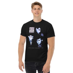 May include: A black short-sleeve t-shirt featuring a graphic print of the band Soda Stereo. The design includes the text "SODA STEREO" in white at the top and "GIRA NADA PERSONAL '85" at the bottom, with blue-toned portraits of three band members.