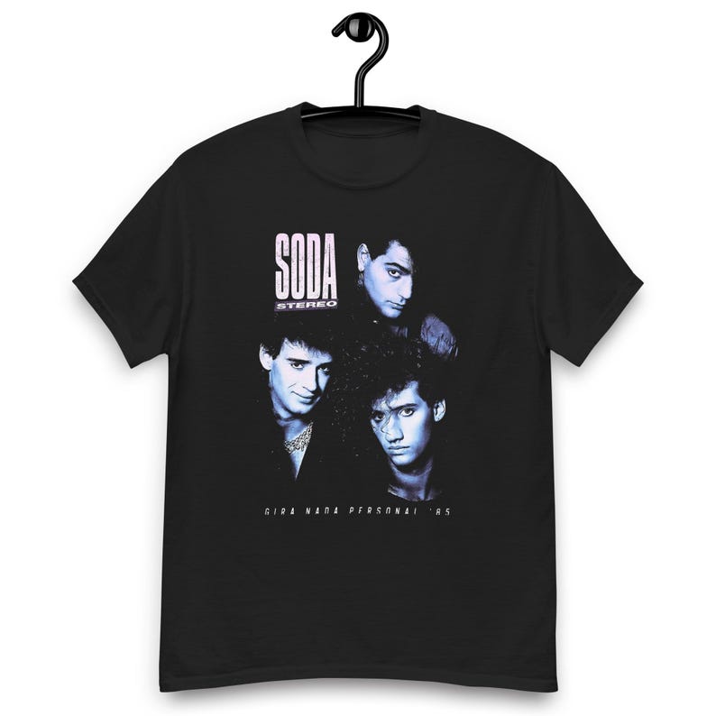 May include: A black short-sleeve t-shirt featuring a blue-toned graphic print of three individuals. The text SODA STEREO is printed in white above the figures, and the text GIRA NADA PERSONAL '85 is printed in white below the figures on the chest.