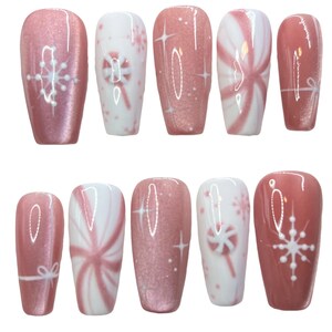 May include: A set of ten artificial nails in various designs. The nails feature a pink and white color scheme with snowflake, star, and candy cane patterns. Some nails have a glittery finish, while others are solid pink or white.