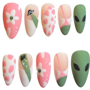 May include: A set of ten artificial nails with various designs. The nails feature pink, white, and green colors. Designs include a flower with an alien face, a UFO, pink spots, and an alien face.
