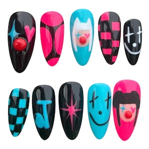 May include: A collection of ten artificial nails with diverse designs. The nails showcase black, pink, and blue hues, adorned with patterns such as hearts, stars, checkerboard, and clown faces. Each nail has a glossy finish.