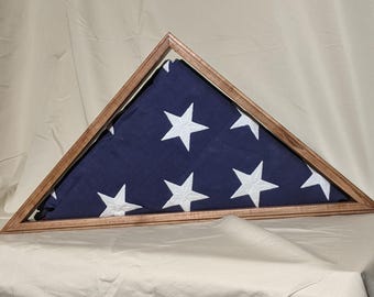 May include: A wooden triangular flag display case with a folded American flag inside. The flag is blue with white stars.