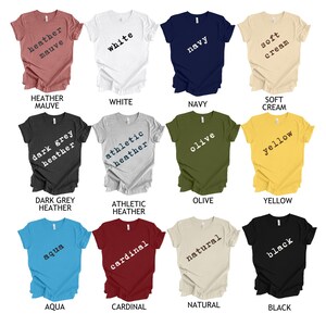 May include: A collection of 12 t-shirts in various colors and styles. The shirts feature different text in a typewriter font, including "heather mauve", "white", "navy", "soft cream", "dark grey heather", "athletic heather", "olive", "yellow", "aqua", "cardinal", "natural", and "black".