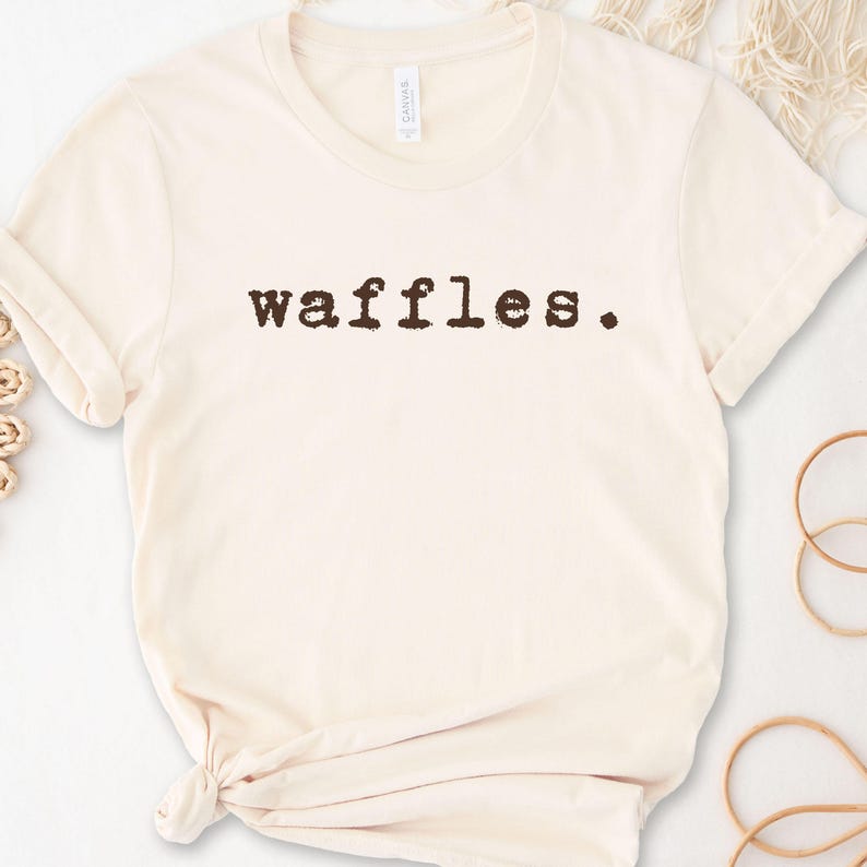 May include: A cream-colored t-shirt with the word "waffles" printed in brown on the front.