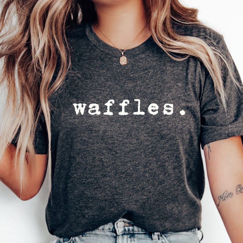 May include: A dark gray t-shirt with the word "waffles" printed in white on the front. The text is in a typewriter font.