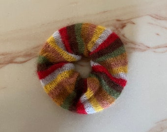 May include: A colorful striped hair scrunchie made of soft, fuzzy yarn. The scrunchie is in shades of red, white, yellow, brown, and green.