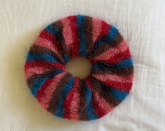 May include: A colorful striped hair scrunchie made of soft, fuzzy yarn in shades of pink, brown, blue, and red.