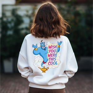 May include: White sweatshirt with a colorful graphic of a blue genie with gold bracelets and a magic lamp. The text "WISH YOU WERE THIS COOL" is printed in a rainbow font.