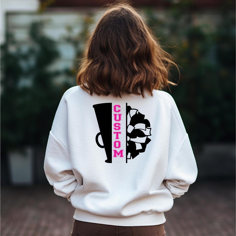 May include: White sweatshirt with a black and white graphic of a cheerleading megaphone and pom poms. The word "CUSTOM" is written vertically in pink on the megaphone.