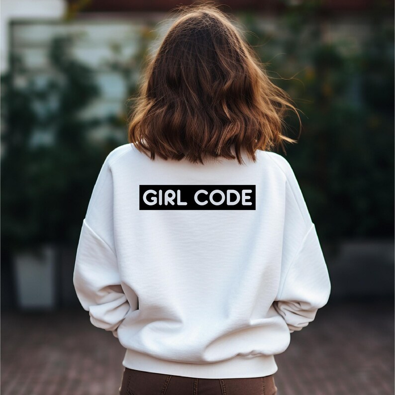 May include: A white sweatshirt with the text "GIRL CODE" in a black rectangle on the back. The person is facing away from the camera, with brown hair.
