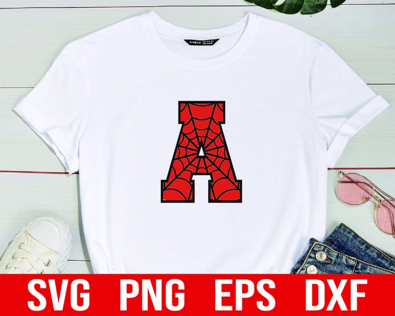 K&ouml;nnte beinhalten: Wei&szlig;es T-Shirt mit einem schwarzen Buchstaben A, gef&uuml;llt mit einem roten und schwarzen Spinnennetz-Design. Das Shirt liegt auf einem wei&szlig;en Holzgrund. SVG, PNG, EPS und DXF Dateien sind unter dem Shirt aufgelistet.